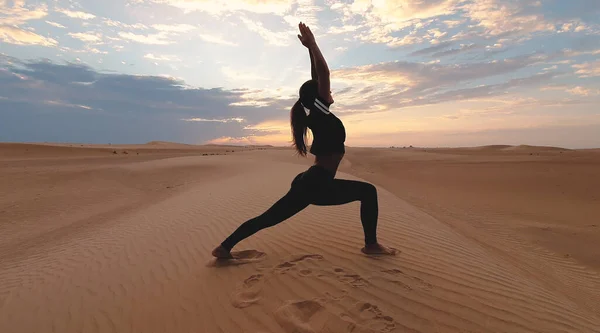 Silhouette of a young woman doing yoga at sunset in the vast desert. Epic sunset and sports concept photo.