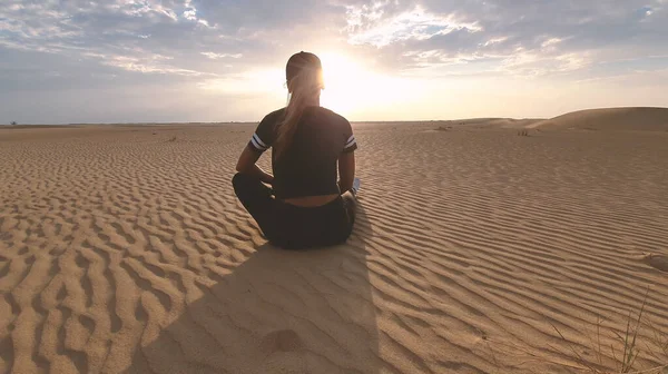 Silhueta de uma jovem mulher fazendo ioga ao pôr do sol no vasto deserto. Pôr do sol épico e foto conceito de esportes. — Fotografia de Stock