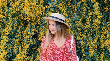 Sarı çiçekli hasır şapkalı sarışın bir kız. Güneşli bir gün ve güzel bir doğa. Moda konsepti.