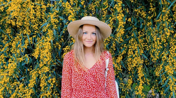 Blond girl in a straw hat on a background of yellow flowers. Sunny day and beautiful nature. Fashion concept. — Stock Photo, Image