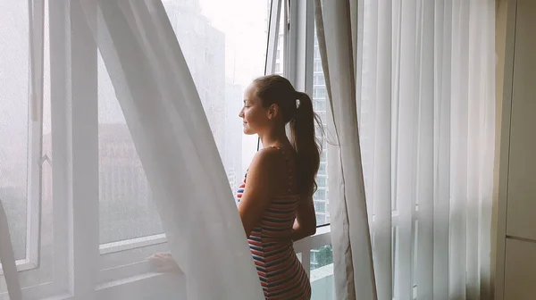 Vista trasera de la mujer mirando por la ventana de la ciudad bajo la lluvia. — Foto de Stock
