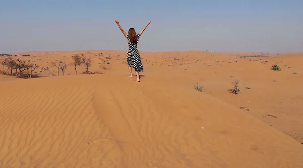AÉRIAL. Femme vêtue d'une longue robe marchant dans les dunes de sable du désert de Dubaï avec des pas dans le sable au coucher du soleil — Photo