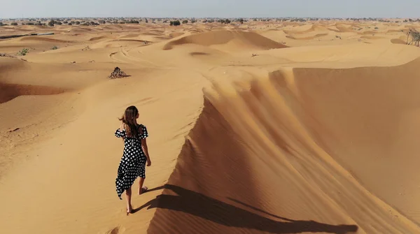 AERIAL. Frau in langem Kleid spaziert in den Sanddünen der Wüste von Dubai und tritt bei Sonnenuntergang in den Sand — Stockfoto