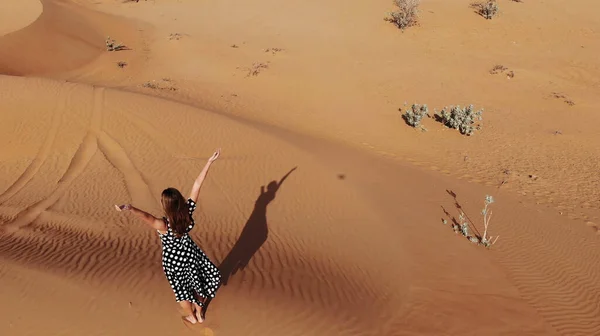 AERIAL. Mulher vestida em vestido longo andando nas dunas de areia do deserto do Dubai com passos na areia durante o pôr do sol — Fotografia de Stock