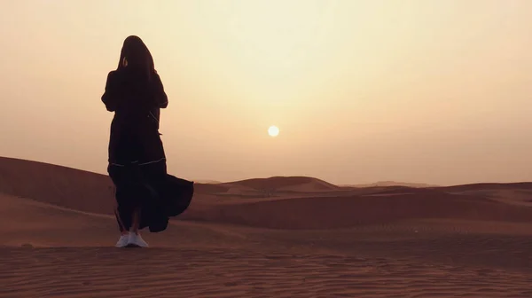 Çölde gün batımında geleneksel siyah kıyafetler giyen genç bir Arap kadının portresi..