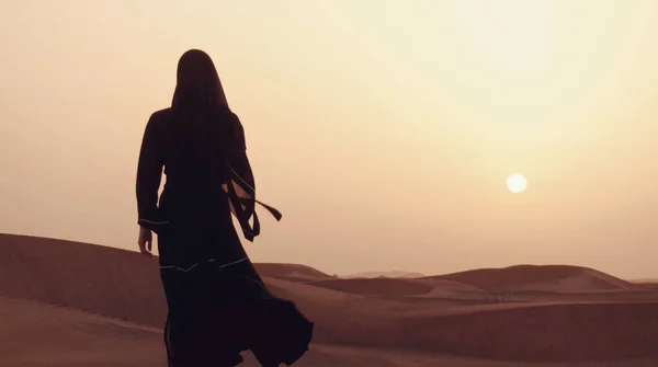 Çölde gün batımında geleneksel siyah kıyafetler giyen genç bir Arap kadının portresi..