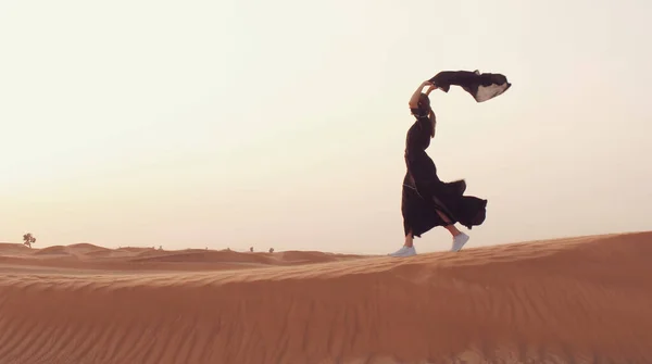 Retrato de uma jovem árabe vestindo roupas pretas tradicionais durante o belo pôr do sol sobre o deserto. — Fotografia de Stock