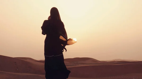 Çölde gün batımında geleneksel siyah kıyafetler giyen genç bir Arap kadının portresi..