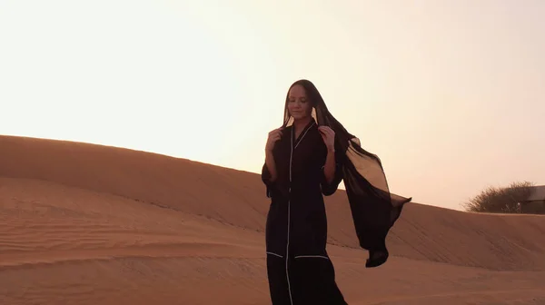 Çölde gün batımında geleneksel siyah kıyafetler giyen genç bir Arap kadının portresi..