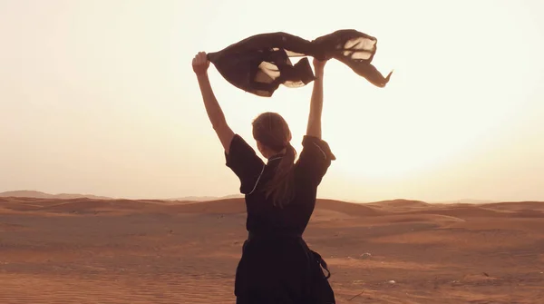 Retrato de uma jovem árabe vestindo roupas pretas tradicionais durante o belo pôr do sol sobre o deserto. — Fotografia de Stock