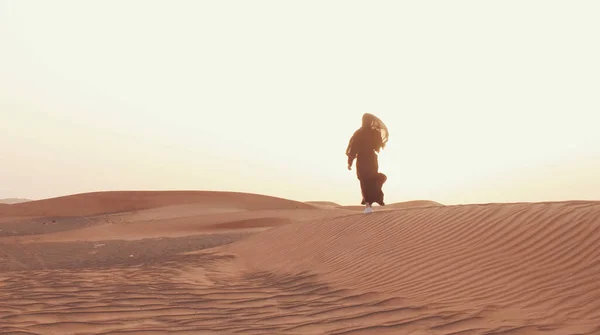 Çölde gün batımında geleneksel siyah kıyafetler giyen genç bir Arap kadının portresi..