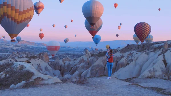 Sırt çantalı kadın yolcu hava balonlarına bakıyor. Sportif kız ve bir sürü sıcak hava balonu. Tam özgürlük, başarı, başarı, mutluluk hissi.