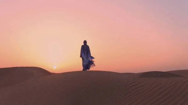 Retrato de una hermosa mujer árabe vestida con un vestido azul tradicional en el desierto al atardecer. — Foto de Stock