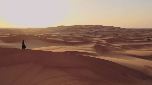 Vista aérea desde un dron volando junto a una mujer en abaya Vestido tradicional de los Emiratos Árabes Unidos caminando por las dunas en el desierto del Barrio Vacío. Abu Dhabi, Emiratos Árabes Unidos. — Foto de Stock