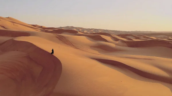 Vista aérea desde un dron volando junto a una mujer en abaya Vestido tradicional de los Emiratos Árabes Unidos caminando por las dunas en el desierto del Barrio Vacío. Abu Dhabi, Emiratos Árabes Unidos. — Foto de Stock