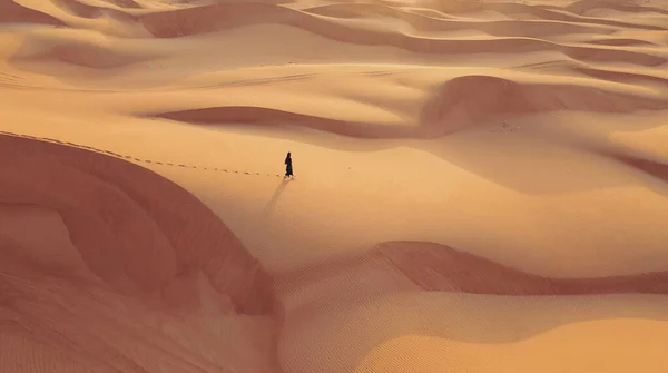 Вид с воздуха с беспилотника, летящего рядом с женщиной в Абайе, Объединенные Арабские Эмираты, традиционное платье, прогуливающееся по дюнам пустыни Пустого квартала. Абу-Даби, ОАЭ. — стоковое фото