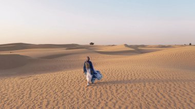 Abaya Birleşik Arap Emirlikleri 'nde bir kadının yanında uçan bir insansız hava aracının hava görüntüsü. Boş Bölge' nin çölünde kumullarda yürüyen geleneksel bir elbise. Abu Dabi, BAE.