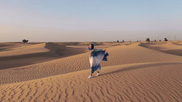 Vista aérea de um drone voando ao lado de uma mulher em abaya Emirados Árabes Unidos vestido tradicional andando sobre as dunas no deserto do Bairro Vazio. Abu Dhabi, EAU. — Fotografia de Stock