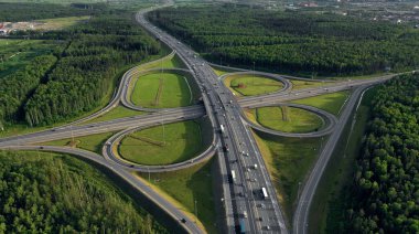 AERİAL. Trafik kavşağı. Yol, şehir ve orman manzaralı. İnsansız hava aracından yaz videosu.