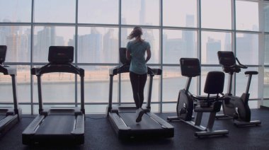 Gün doğumunda şehir manzaralı panoramik pencerede koşu bandında koşan bir kadın..