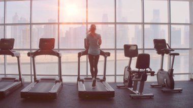 Gün doğumunda şehir manzaralı panoramik pencerede koşu bandında koşan bir kadın..