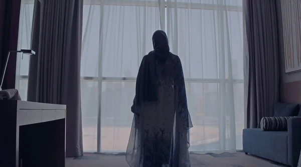 Visão traseira da mulher abrindo cortinas e olhando de janela em paisagem urbana no hotel pela manhã. Edifícios modernos na cidade de Dubai — Fotografia de Stock