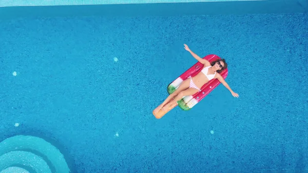 AÉRIAL. Charmante jeune femme caucasienne blonde en lunettes de soleil et maillot de bain nage sur un matelas gonflable dans la piscine avec vue magnifique sur la mer — Photo