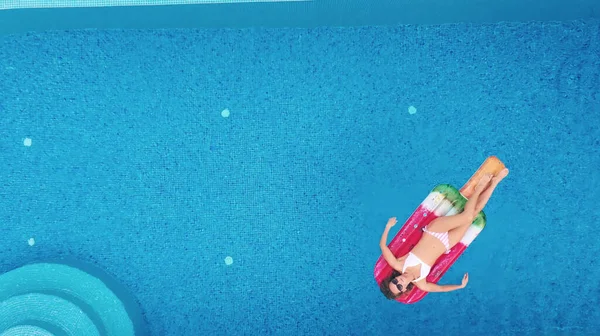 AERIAL. Encantadora joven mujer blanca rubia en gafas de sol y traje de baño nada en un colchón de aire en la piscina con magníficas vistas al mar —  Fotos de Stock