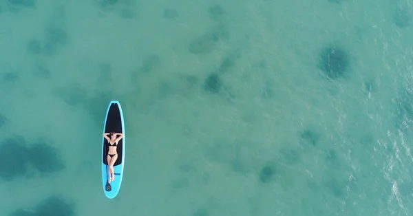 Atrakcyjna kobieta w bikini opala się na desce surfingowej, widok z lotu ptaka — Zdjęcie stockowe
