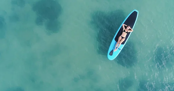 Aantrekkelijke vrouw in bikini is zonnebaden op een surfplank, vanuit de lucht bekeken — Stockfoto