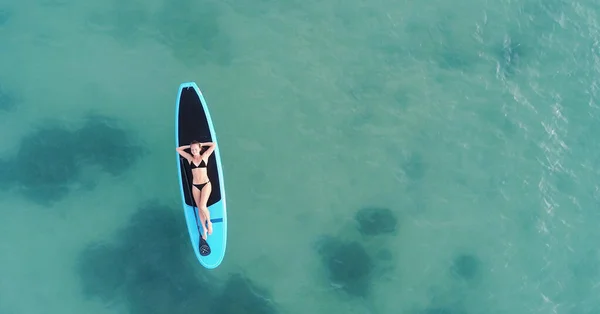 Aantrekkelijke vrouw in bikini is zonnebaden op een surfplank, vanuit de lucht bekeken — Stockfoto