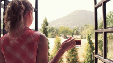 Dağ manzarası. Genç ve güzel bir kız evdeki tropikal bahçede sabah kahvesini yudumluyor..