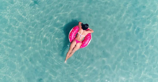 AÉRIAL. Vue du dessus de la jeune fille assez sexy nageant avec matelas de natation rose à l'océan, portant un bikini et des lunettes de soleil, vue sur l'océan, se détendre et s'amuser en vacances. — Photo