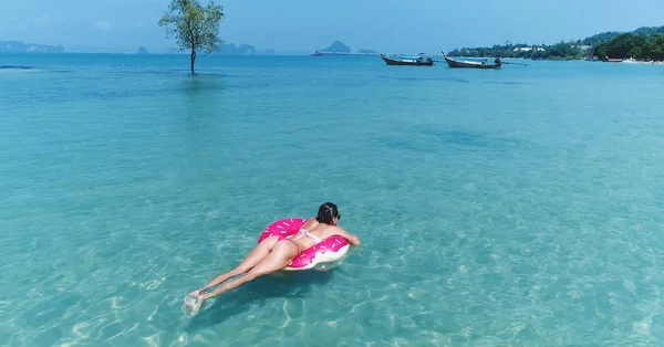 AERIAL. Vista superior de la joven chica bastante sexy nadando con colchón de natación rosa en el océano, usando bikini y gafas de sol, vista al mar, relajarse y divertirse en vacaciones. — Foto de Stock