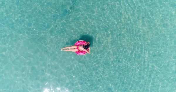 AÉRIAL. Vue du dessus de la jeune fille assez sexy nageant avec matelas de natation rose à l'océan, portant un bikini et des lunettes de soleil, vue sur l'océan, se détendre et s'amuser en vacances. — Photo