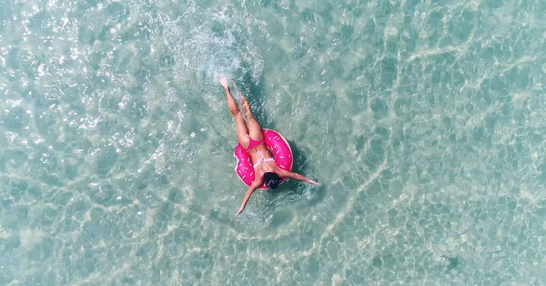 AERIAL. Visão superior da jovem menina muito sexy nadando com colchão de natação rosa no oceano, vestindo biquíni e óculos de sol, vista sobre o oceano, relaxar e se divertir em férias. — Fotografia de Stock