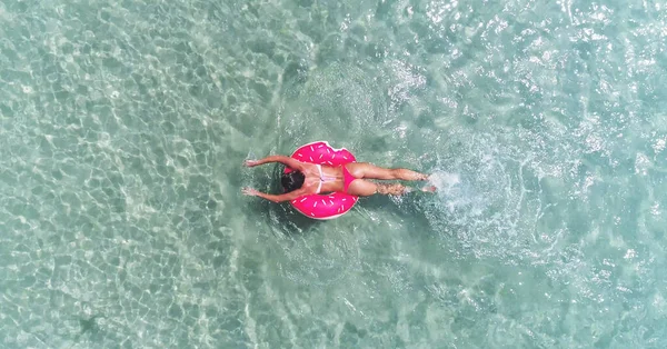AERIAL. Visão superior da jovem menina muito sexy nadando com colchão de natação rosa no oceano, vestindo biquíni e óculos de sol, vista sobre o oceano, relaxar e se divertir em férias. — Fotografia de Stock