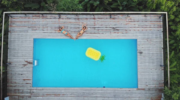 L'air. Drone photo de deux belles filles sexy dans un élégant maillot de bain relaxant au bord de la piscine dans une villa de luxe — Photo