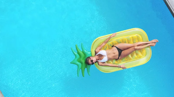 Ananas şekilli şişme yatakta yüzen bir kadının havuz manzarası..