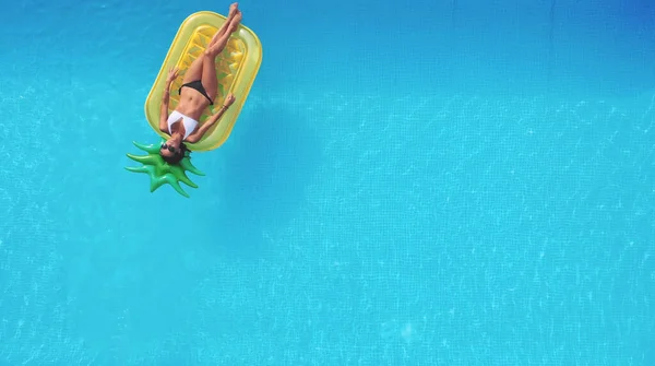 Ananas şekilli şişme yatakta yüzen bir kadının havuz manzarası..