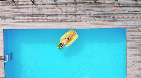 Vista aérea da mulher no colchão inflável em forma de abacaxi na piscina. — Fotografia de Stock