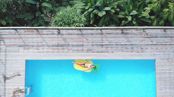 Ananas şekilli şişme yatakta yüzen bir kadının havuz manzarası.. — Stok fotoğraf