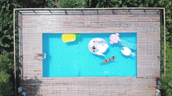 AERİAL. Havuzdaki şişme yatakta eğlenen bir kadın. Çeşitli renk ve şekillerde farklı şişirilebilir yataklar.