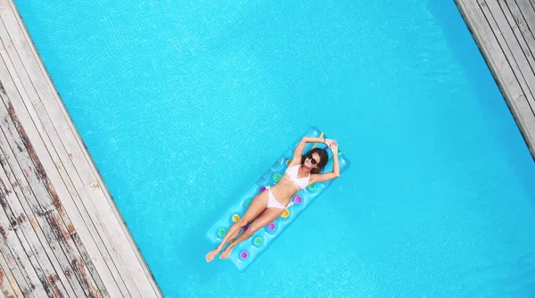 AÉRIAL. Vue de dessus. Style de vie en plein air portrait en gros plan de jeune jolie fille sexy posant avec matelas lumineux néon à la piscine, portant un bikini et des lunettes de soleil, se détendre et s'amuser en vacances. — Photo