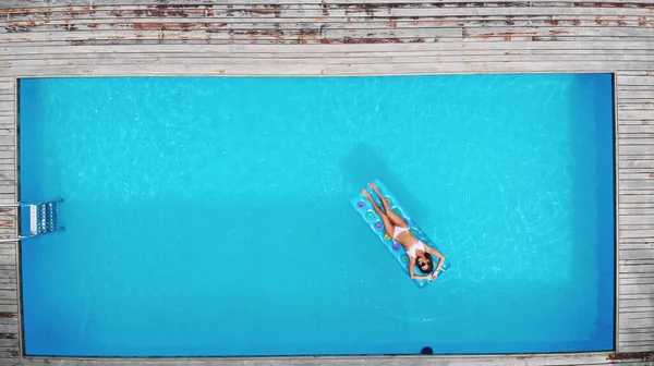 AÉRIAL. Vue de dessus. Style de vie en plein air portrait en gros plan de jeune jolie fille sexy posant avec matelas lumineux néon à la piscine, portant un bikini et des lunettes de soleil, se détendre et s'amuser en vacances. — Photo