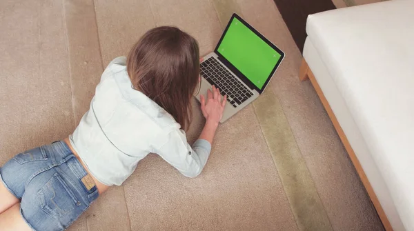 Rilassarsi a casa. Bella giovane donna che utilizza il suo computer portatile mentre si trova sul tappeto a casa. Schermo verde. — Foto Stock