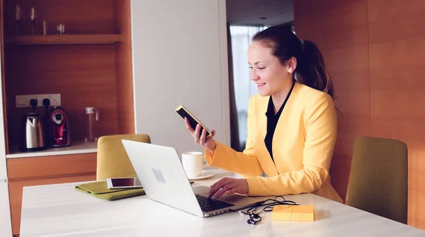 Νέα όμορφη γυναίκα φορώντας ένα κίτρινο σακάκι κάθεται σε μια καρέκλα γραφείου, ενώ χρησιμοποιώντας ένα φορητό υπολογιστή. — Φωτογραφία Αρχείου