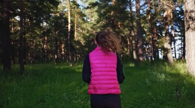 Spor kıyafetleri giyen ve baharda dağdaki yeşil ormanda koşan güzel bir kız.
