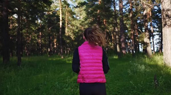 Spor kıyafetleri giyen ve baharda dağdaki yeşil ormanda koşan güzel bir kız.