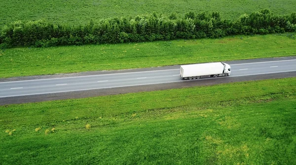 Vrachtwagens die naar de zon rijden. Luchtfoto van groene velden en vrachtwagens — Stockfoto